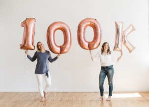 two women celebrating 100k in sales with 100k balloons