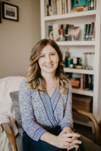 headshot of a woman with brown hair sitting in front of a book shelf
