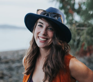 woman with brown hair wearing a hat and smiling at the camera