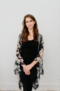 woman with long brown hair standing in front of a white wall