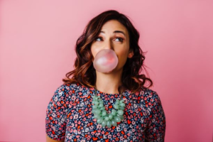 headshot of a woman blowing a pink bubble with pink background